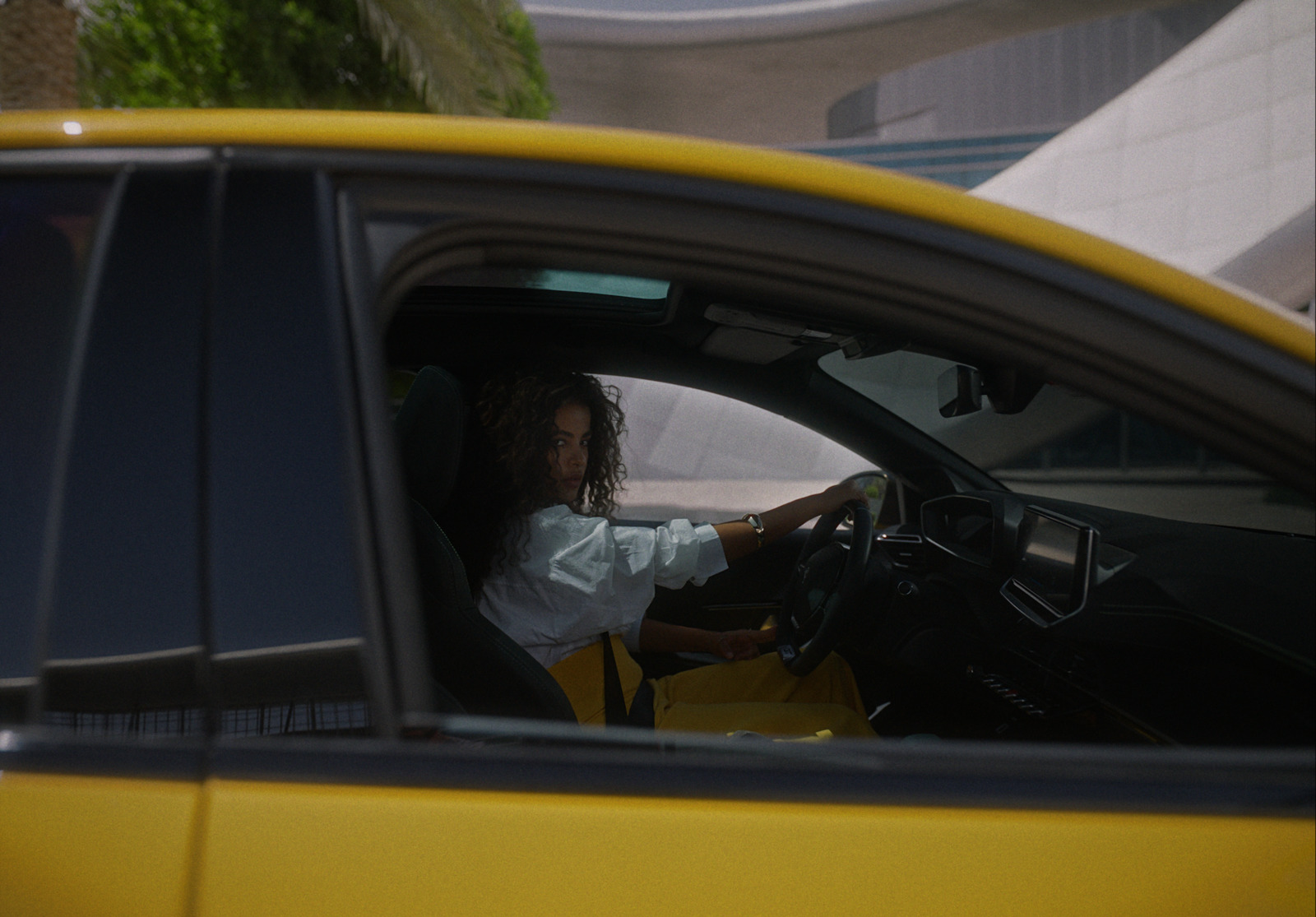 a woman sitting in a yellow car with her hand on the steering wheel