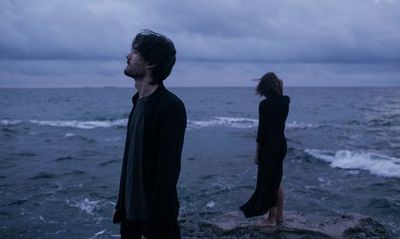 a man and a woman standing on a rock near the ocean