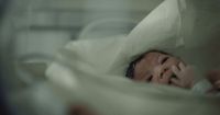 a baby laying in a bed with a white sheet