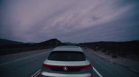 a white car driving down a highway under a cloudy sky