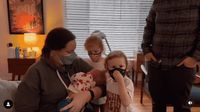 a woman and two children wearing masks in a living room