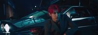 a man with red hair sitting in front of a car