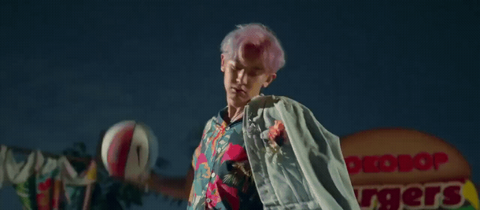 a man with pink hair standing in front of a sign