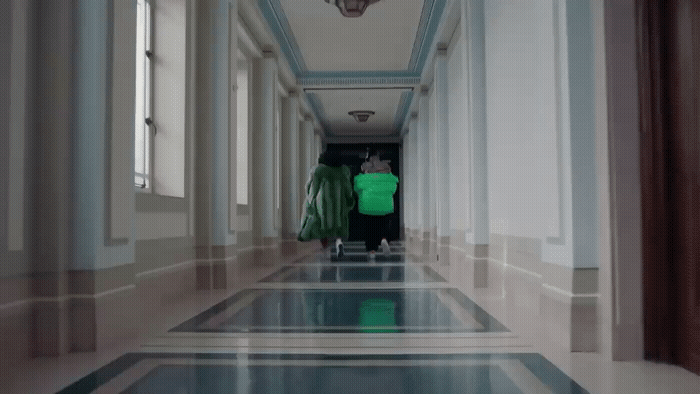 a man in a green jacket walking down a hallway