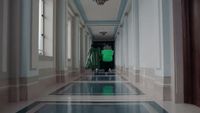 a man in a green jacket walking down a hallway