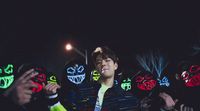 a man standing in front of a group of people wearing neon masks