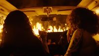 two women sitting in the back of a car in front of a fire