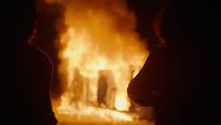two people standing in front of a fire
