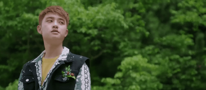 a young man standing in front of a lush green forest