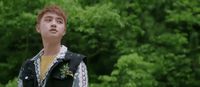 a young man standing in front of a lush green forest