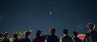 a group of people watching a kite fly in the sky