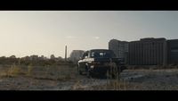 a black truck parked in a field next to tall buildings