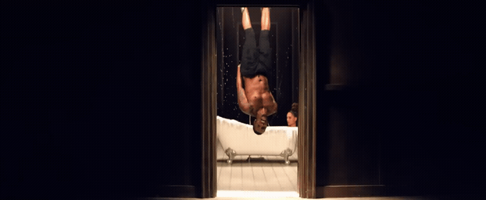a man hanging upside down from a bed in a dark room