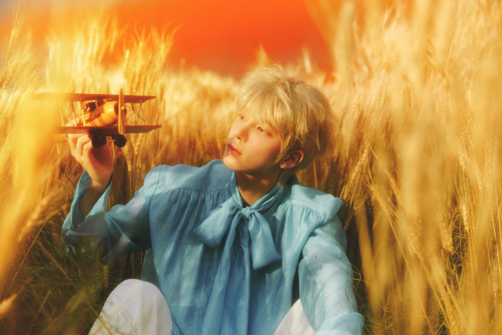 a boy sitting in a field holding a toy airplane