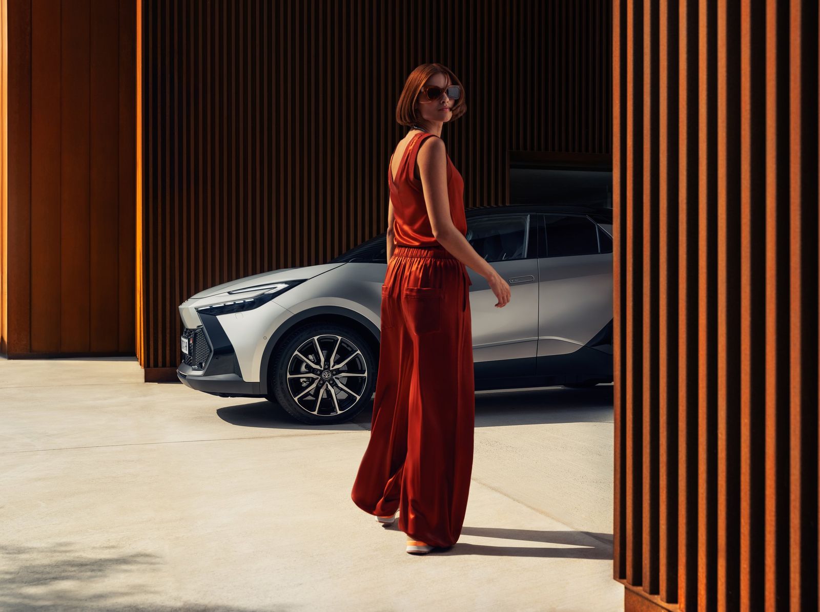 a woman in a red jumpsuit standing next to a car