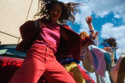 a woman in a pink top and red pants standing next to a car