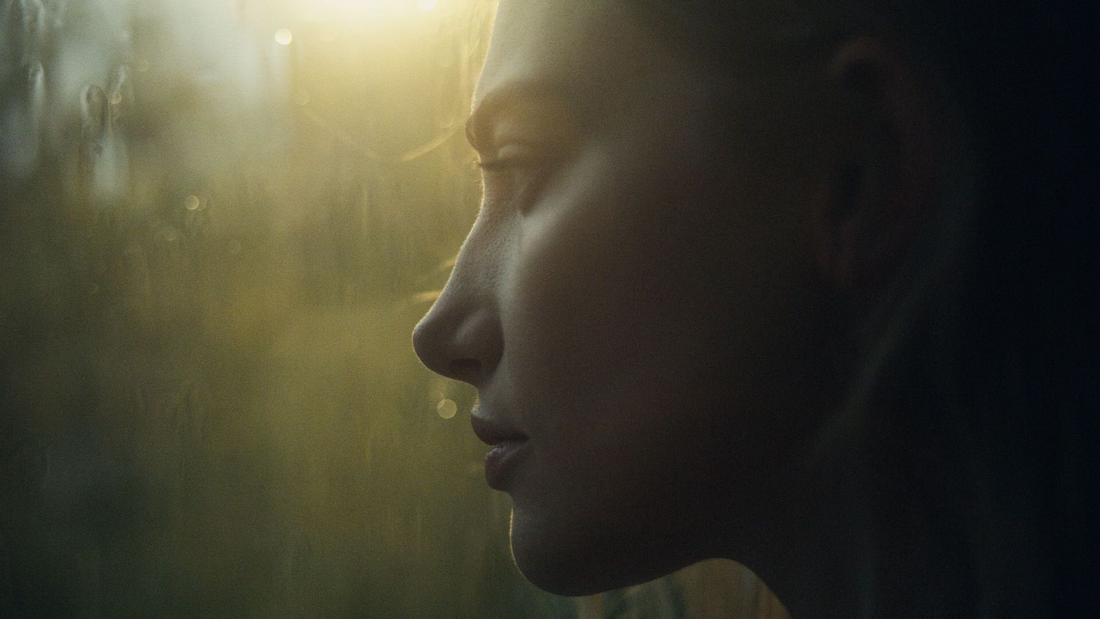 a woman looking out a window at the sun