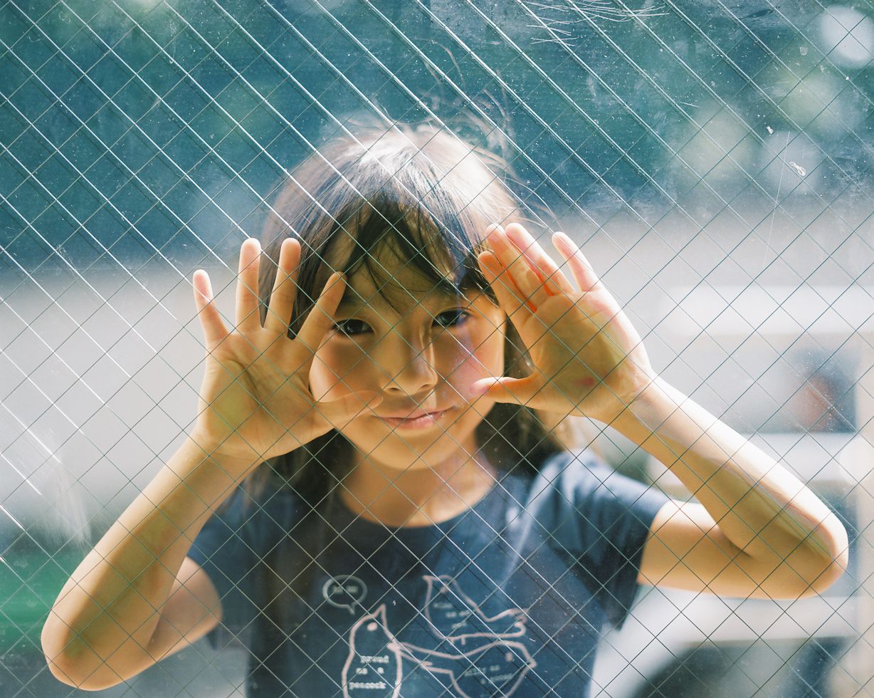 a young girl holding her hands up behind a fence