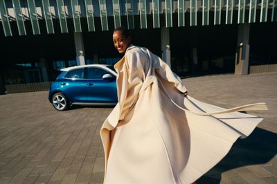 a woman in a white coat and red pants is walking by a blue car