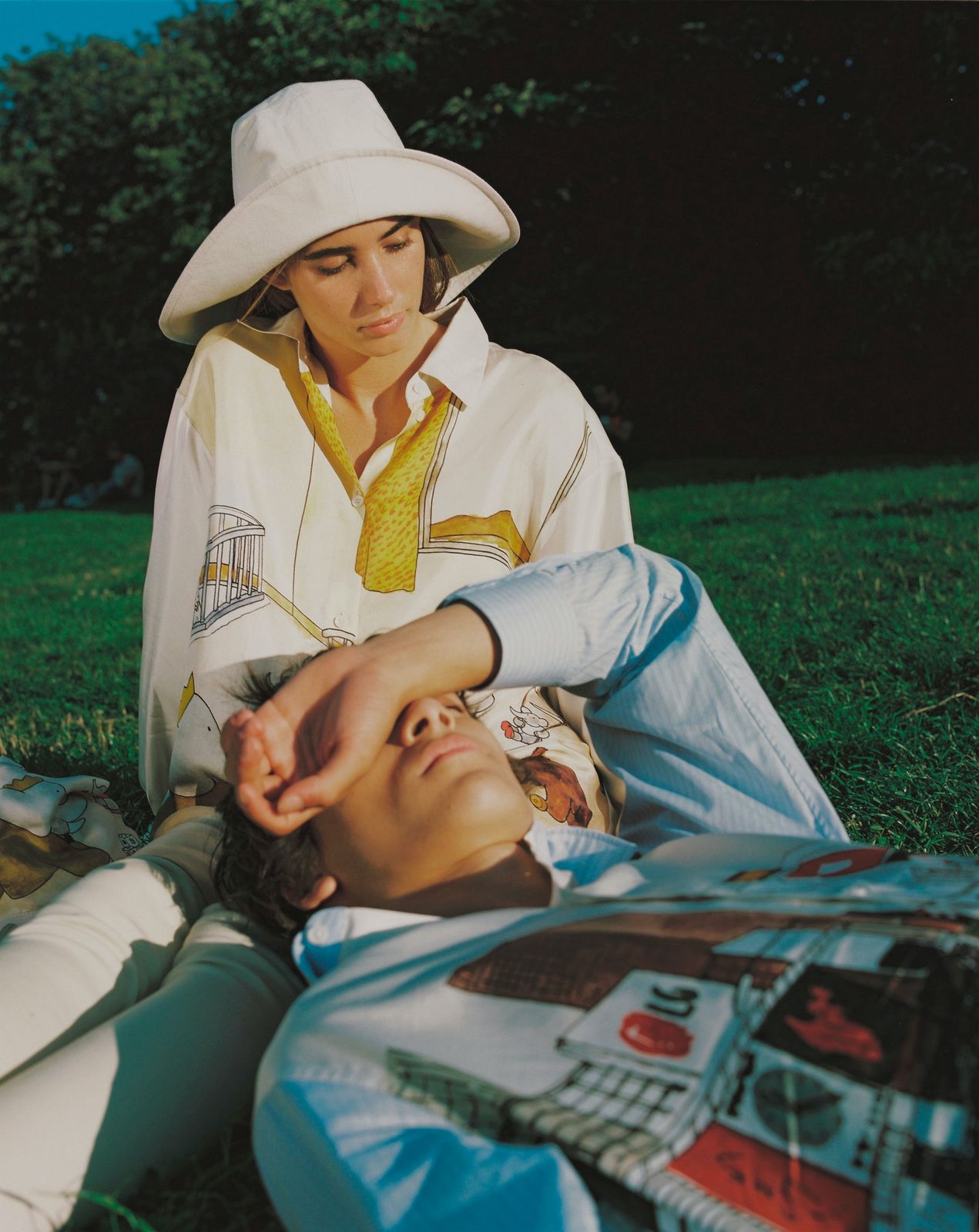 a woman sitting next to a man laying on the ground