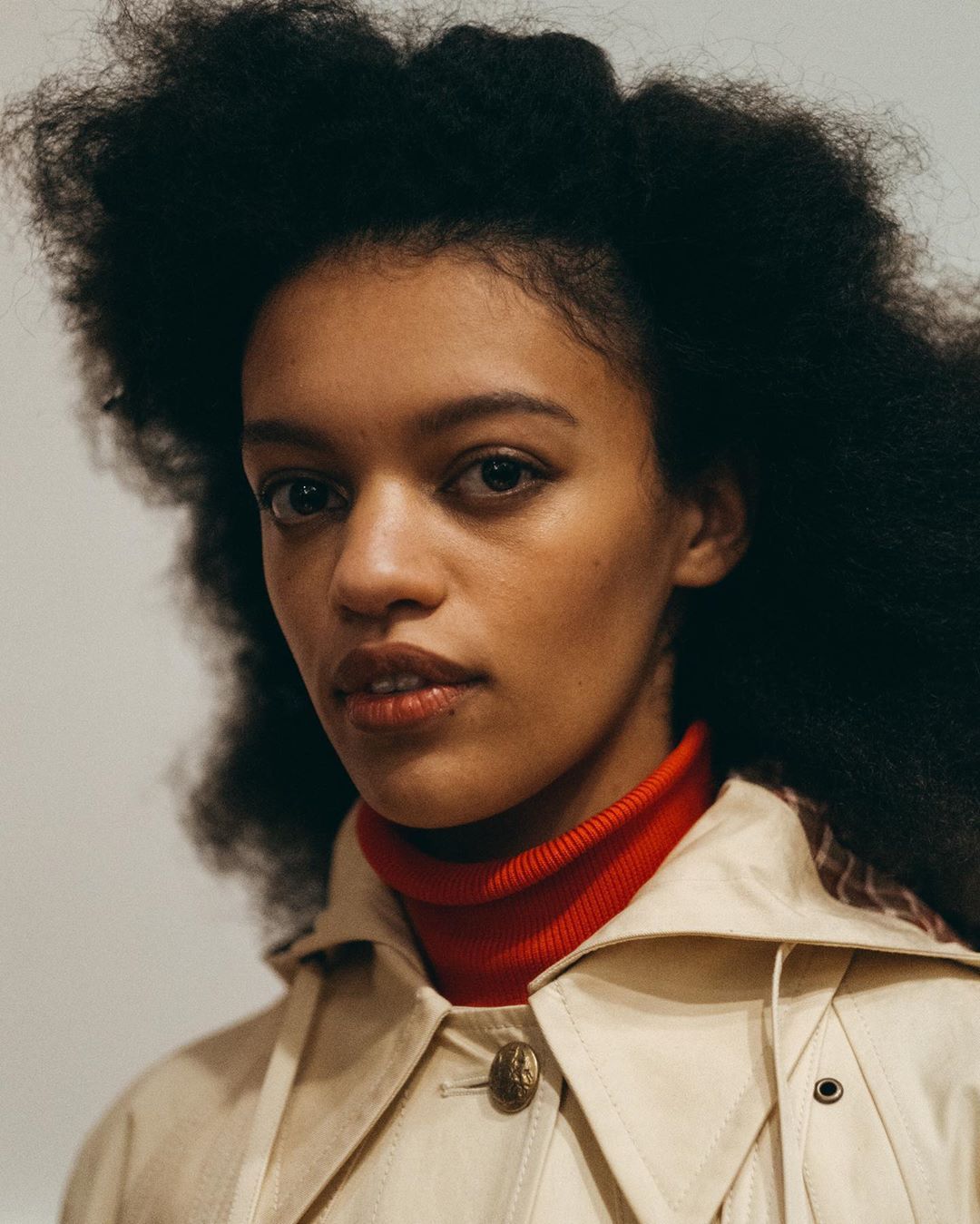 a woman with an afro wearing a trench coat