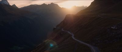 the sun is setting over a mountain road