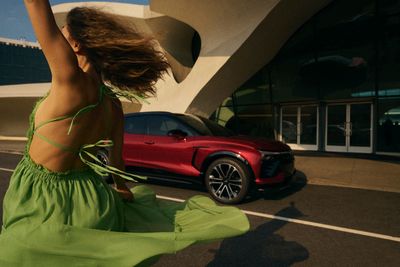 a woman in a green dress dancing in front of a red sports car