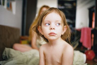 a naked child sitting on a bed with a woman in the background