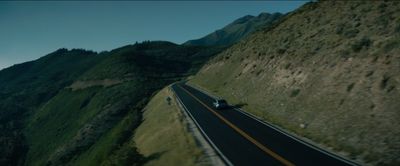 a car driving down a road next to a lush green hillside