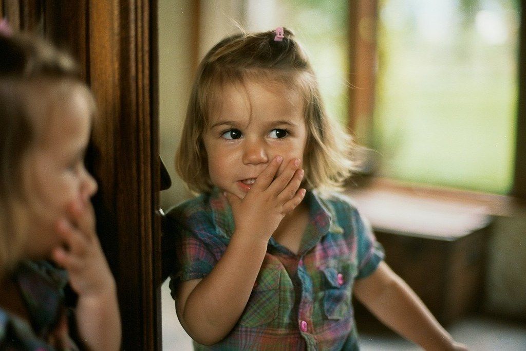 a little girl standing in front of a mirror