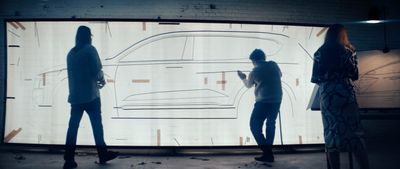 a group of people standing in front of a projection of a car