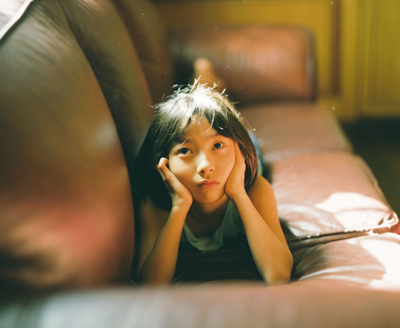 a little girl laying on a couch with her hands on her face