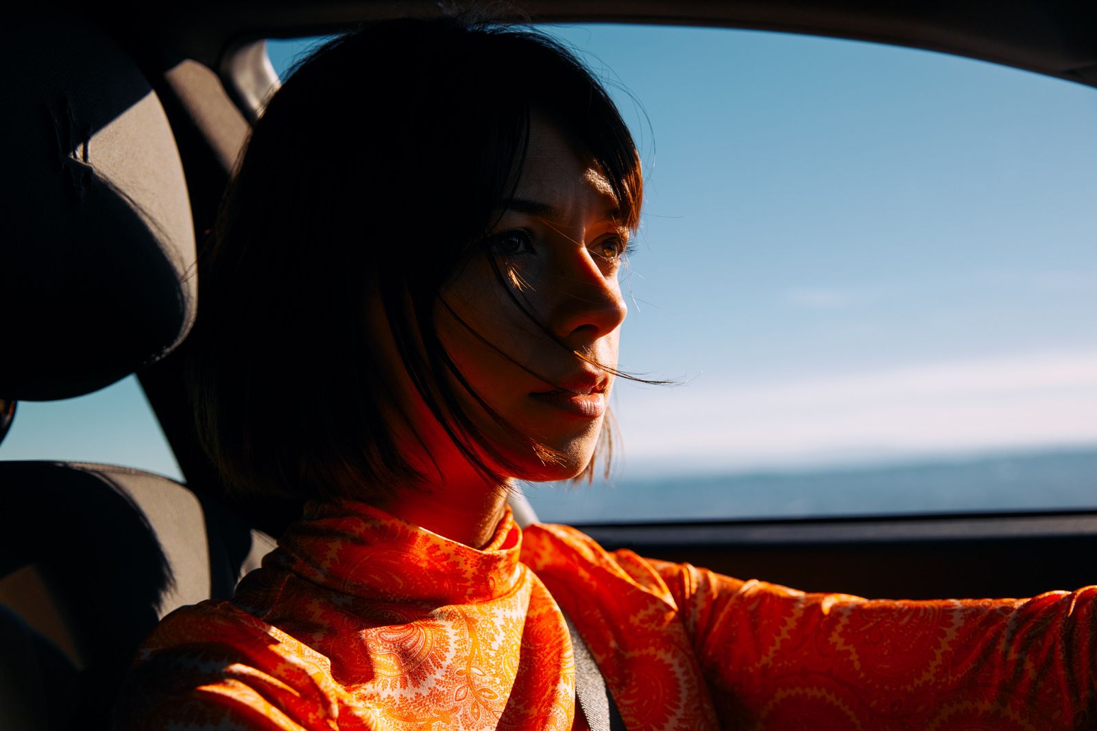 a woman sitting in a car with a scarf around her neck