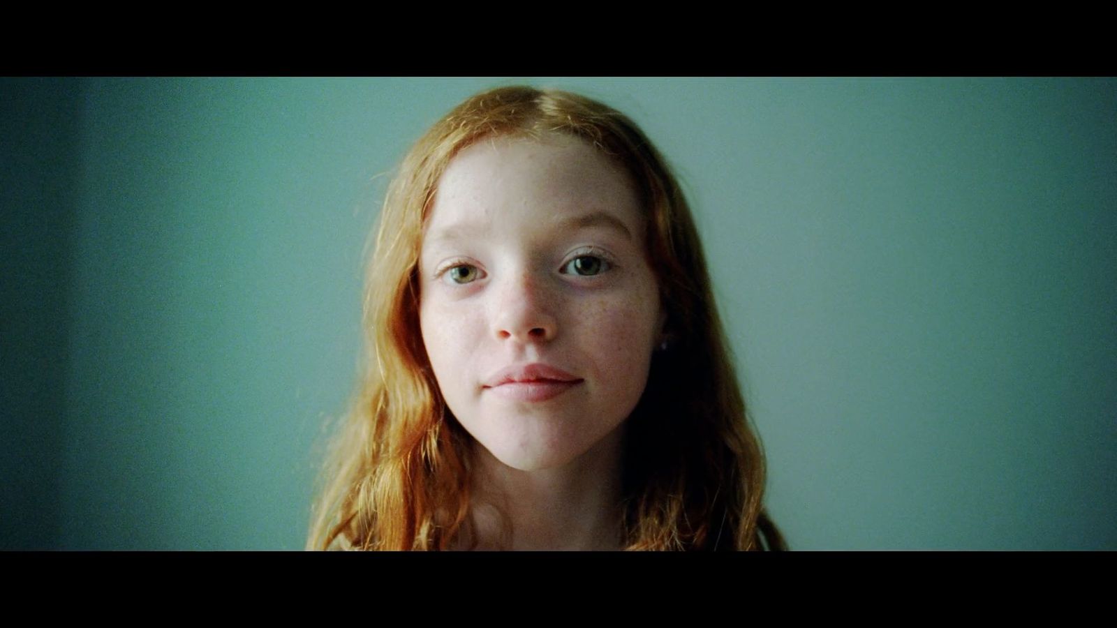 a young girl with red hair is looking at the camera