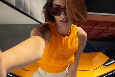 a woman in a yellow top is standing next to a yellow car