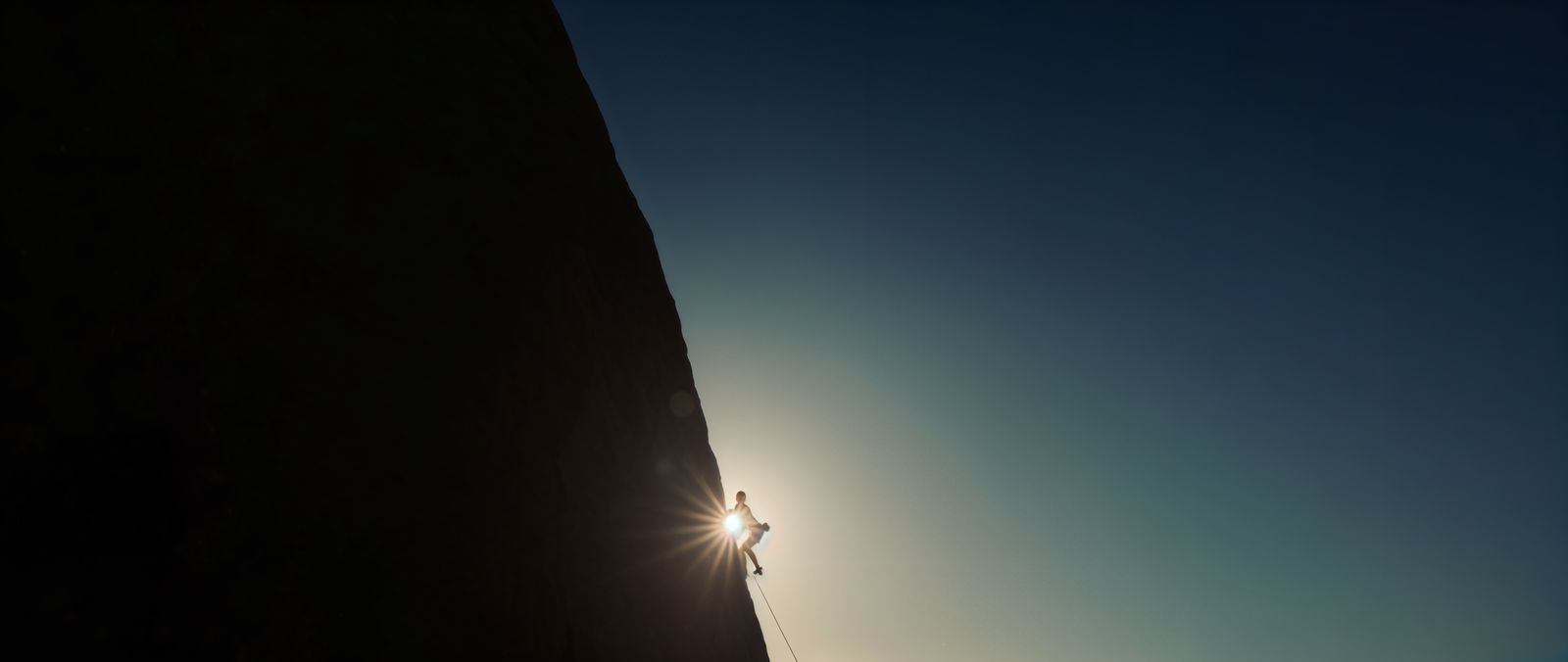 a person climbing up a steep hill with the sun behind them