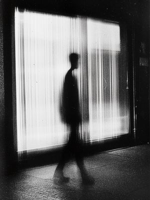 a black and white photo of a person walking in front of a window