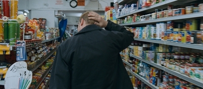 a man in a black jacket is looking at a shelf of food