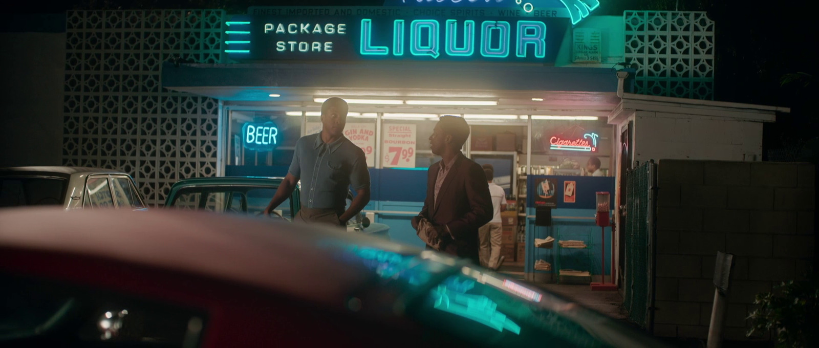 two men standing outside of a liquor store at night