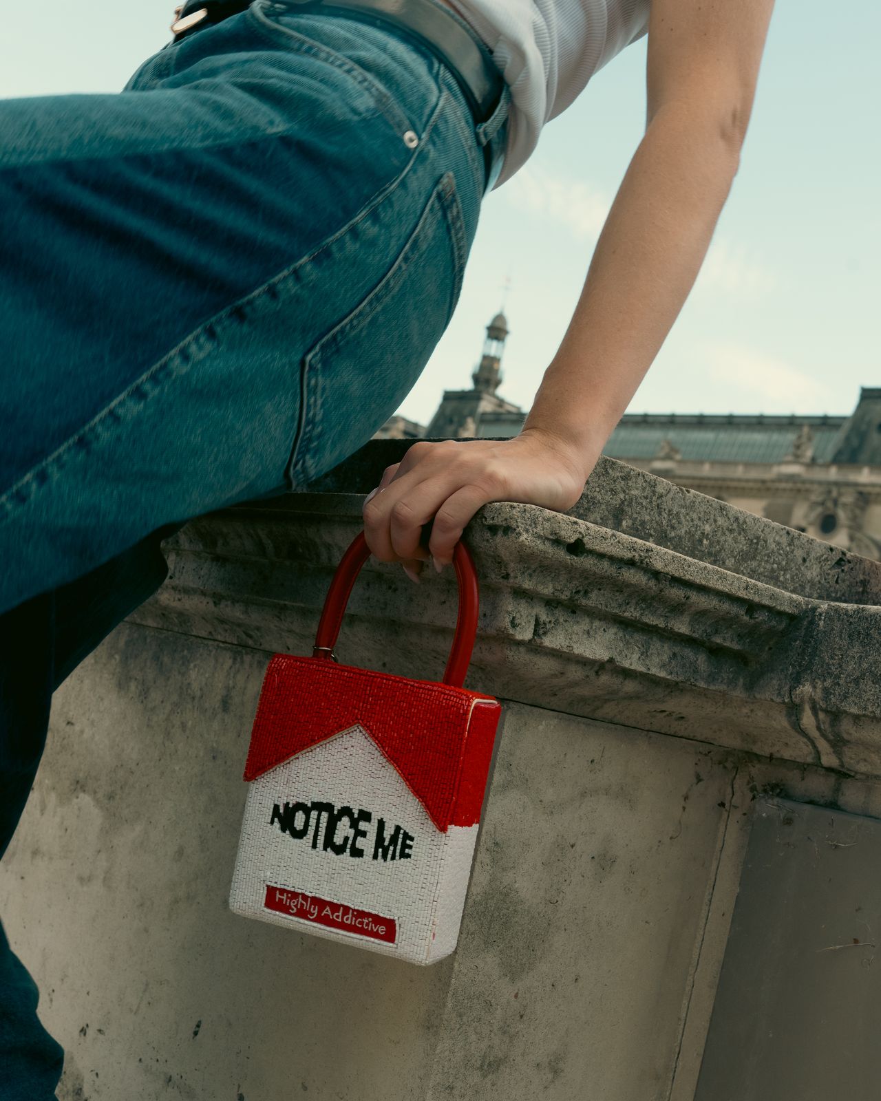 a person sitting on a ledge holding a red bag