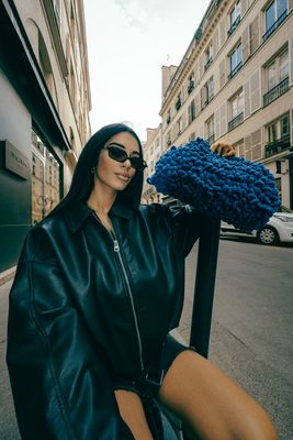 a woman in a black leather jacket and sunglasses sitting on a scooter