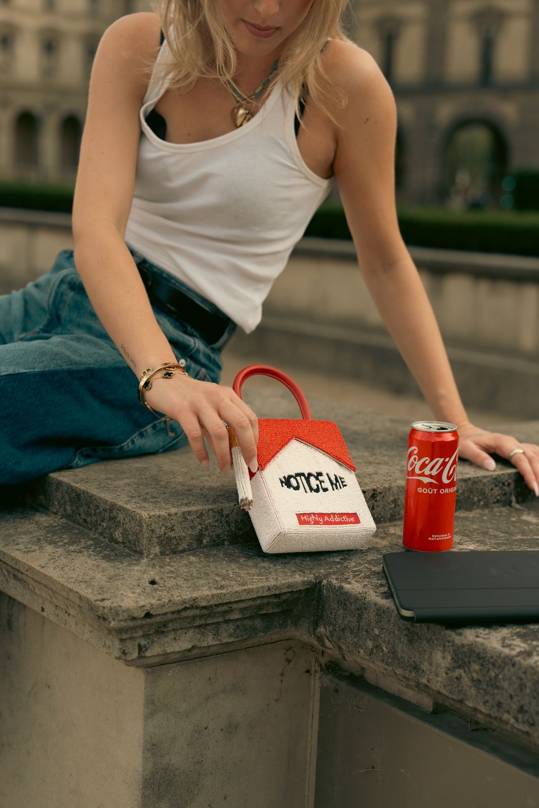 a woman sitting on a ledge with a coca - cola bag