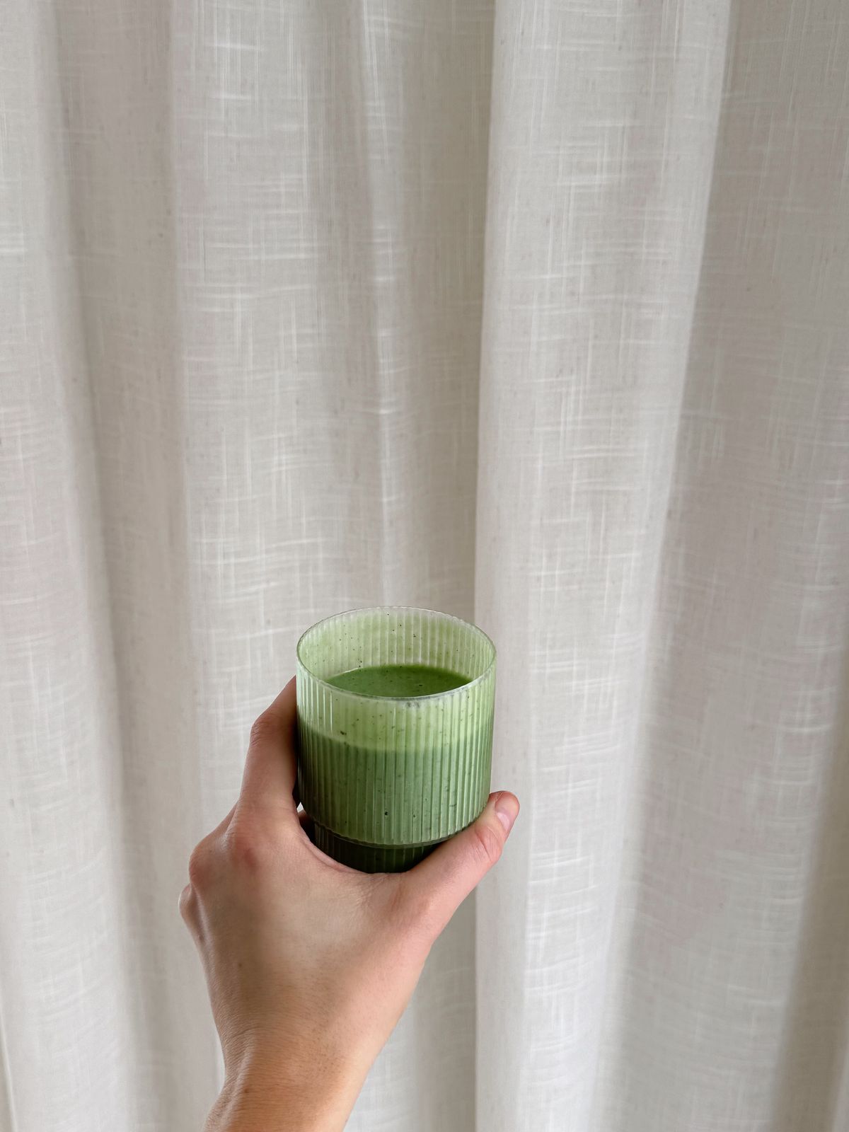 a hand holding a green cup in front of a curtain