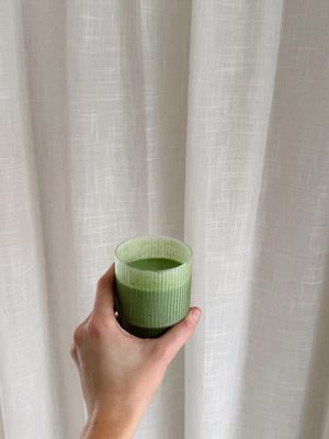 a hand holding a green cup in front of a curtain