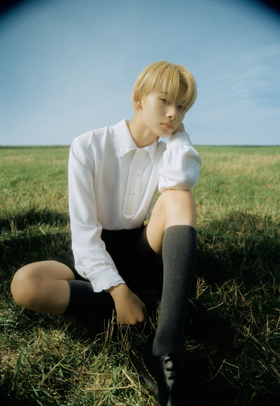 a young man sitting in the grass with his legs crossed