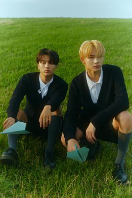 two young men sitting in the grass with paper airplanes