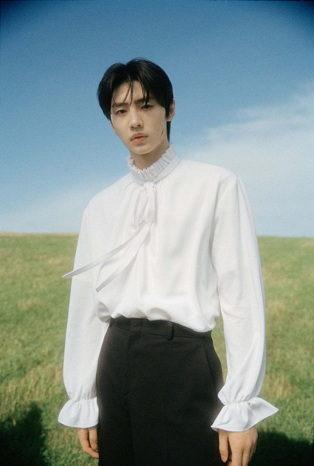 a man standing in a field wearing a white shirt and black pants