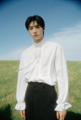 a man standing in a field wearing a white shirt and black pants