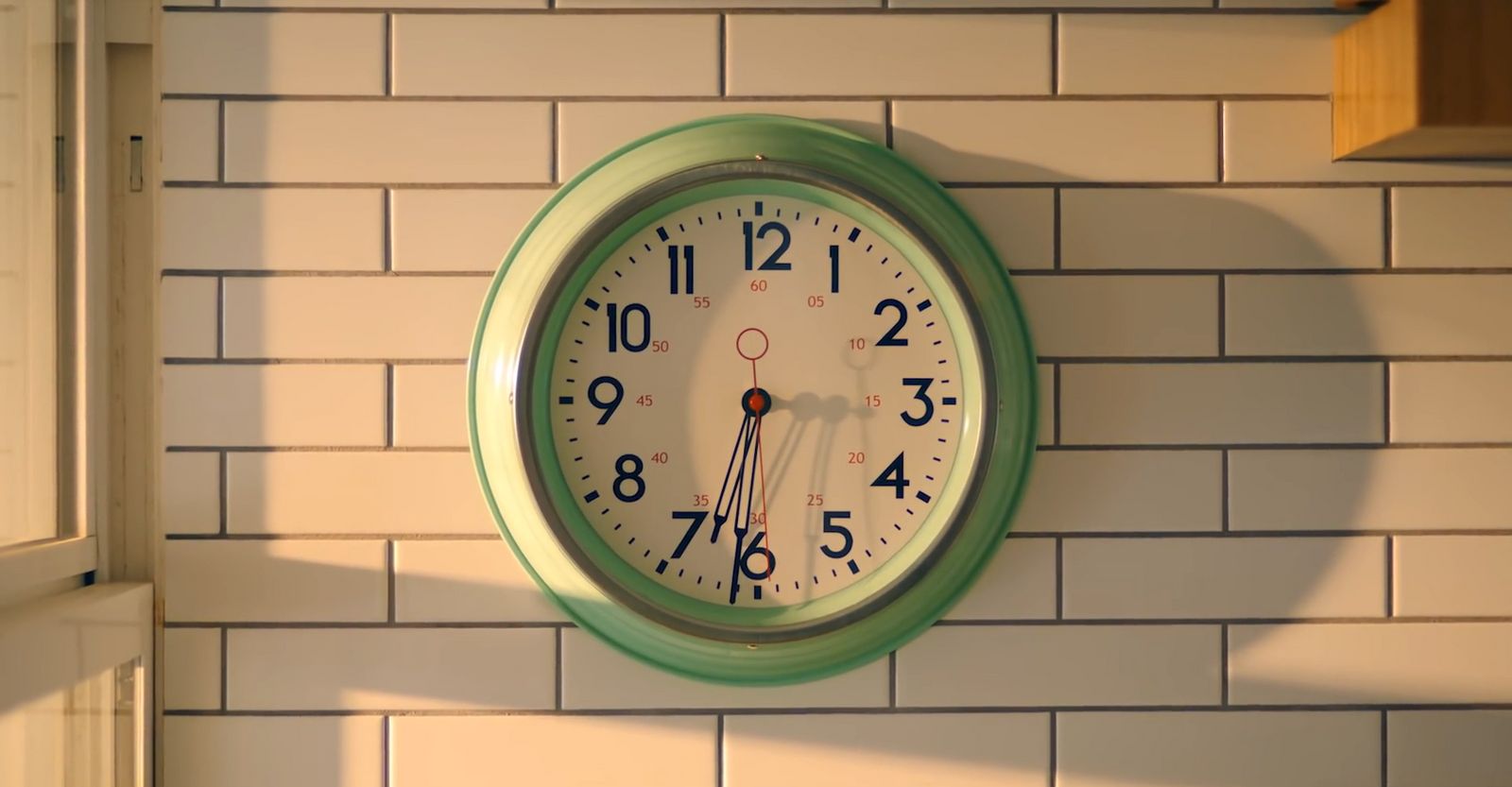 a green clock mounted to the side of a white brick wall