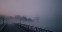 a foggy bridge with street lights and a boat in the distance